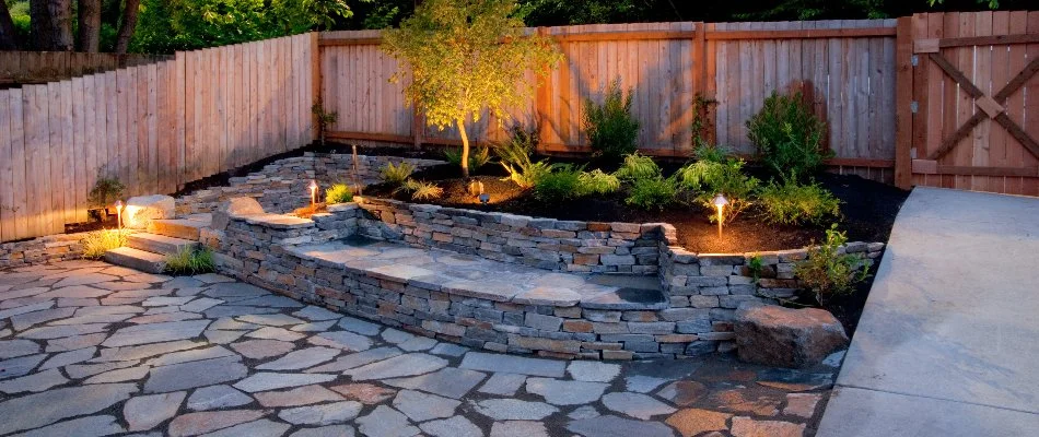 Backyard area in Tarrytown, NY, with a stone wall and lighting.